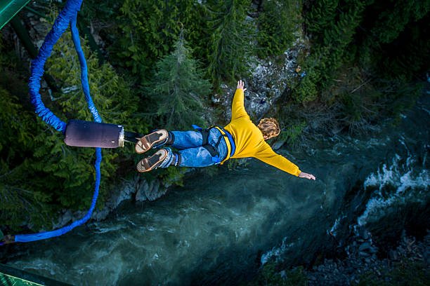 Young man bungee jumping over river.
