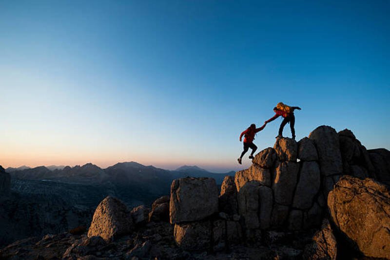 One climber helping the other get to the top of a mountain