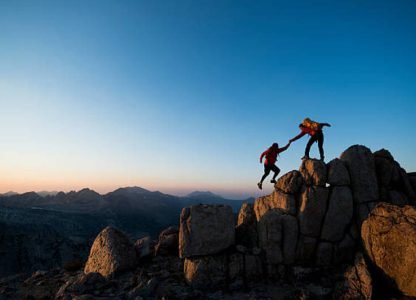 One climber helping the other get to the top of a mountain